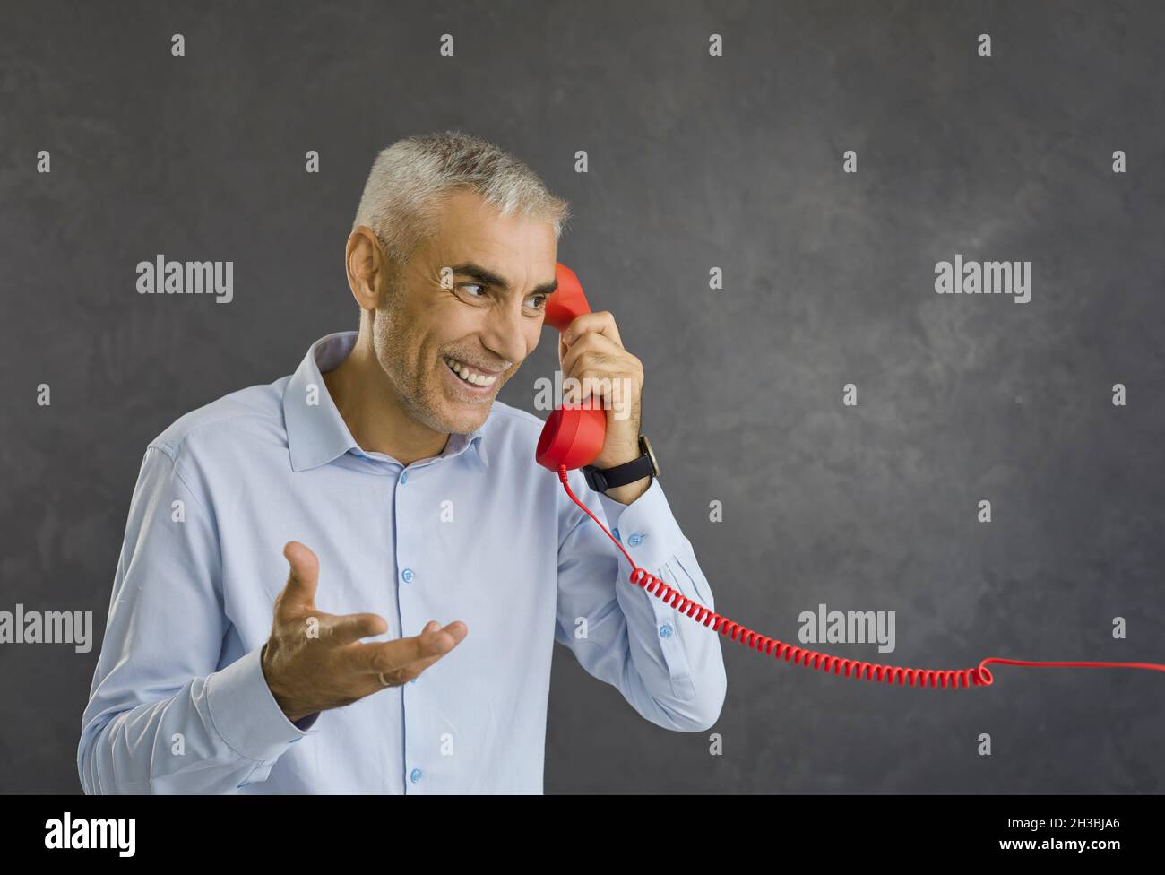 Happy smiling retired senior man talking to someone on red retro landline telephone Stock Photo