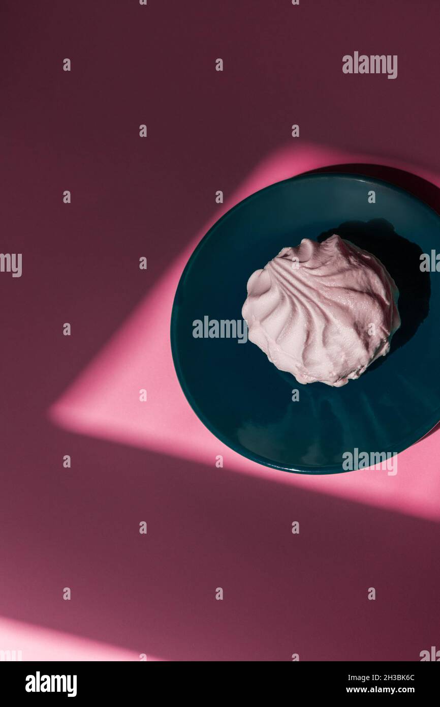 One marshmallow lies on an aqua saucer on a pink background.  Stock Photo