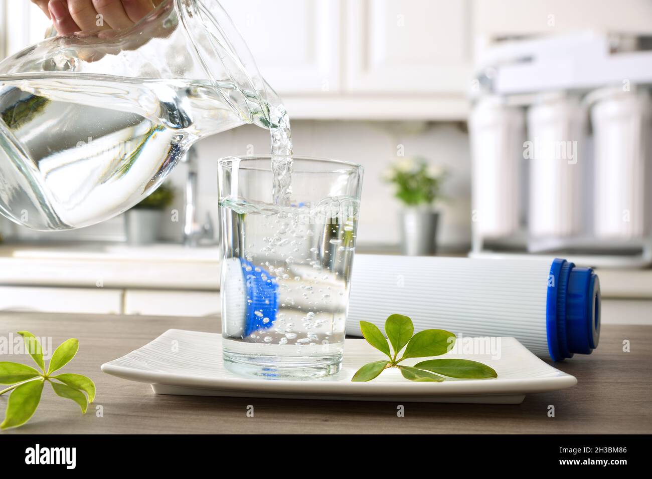 Hand filling crystal glass on kitchen bench from jug with filtered water using reverse osmosis household equipment. Front view. Horizontal composition Stock Photo