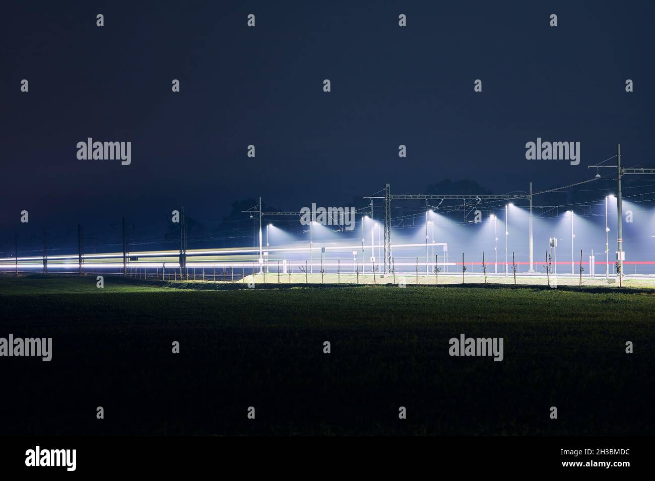 Light trail of train. Traffic on electrified railroad track at night. Stock Photo
