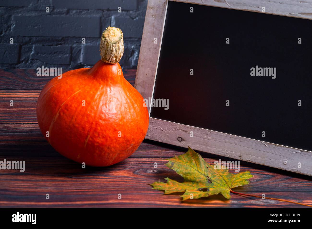 The photo shows an orange Hokkaido pumpkin with a leaf and a chalkboard with black wall Stock Photo