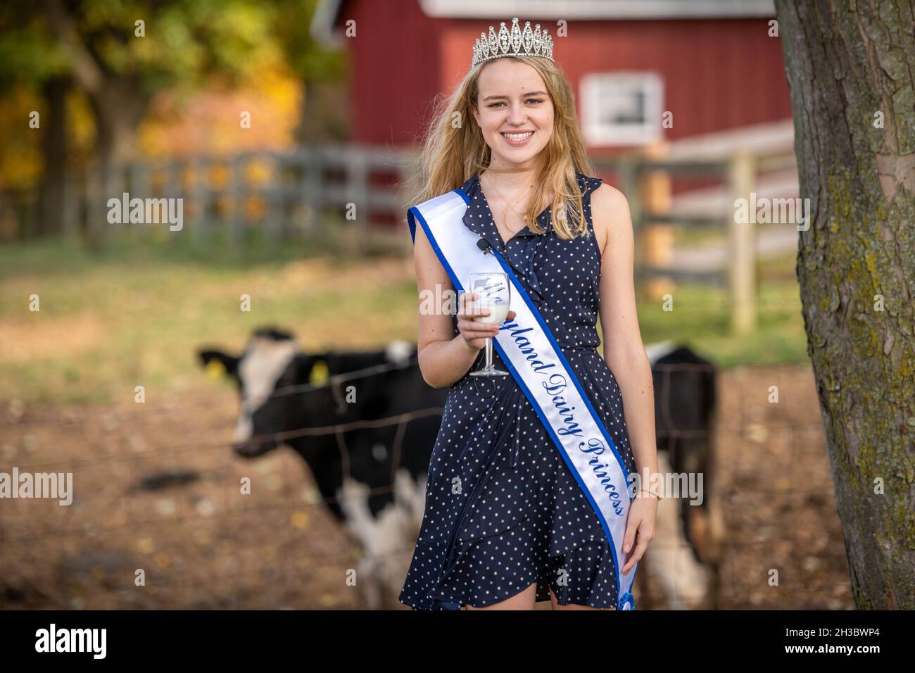 Maryland Dairy Princess smiling with a glass of milk in front of a cow