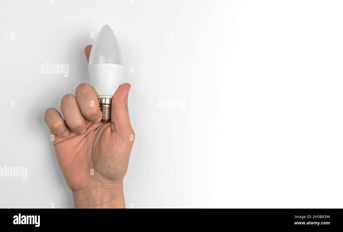 Hand with LED light bulb on a white table background with copy space Stock Photo