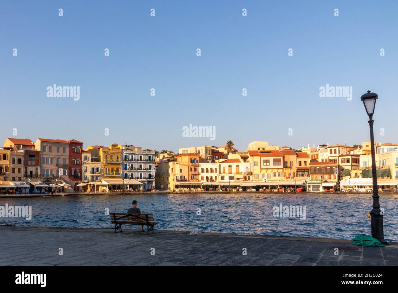 Man sat on a bench in the late afternoon, Old Venetian Harbour, Chania, Crete, Greece Stock Photo