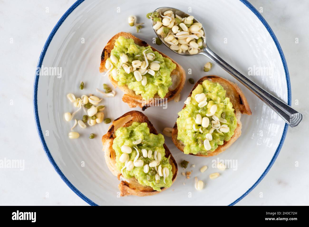 Vegan toasts with mashed avocado and mung bean sprouts on white plate, top view Stock Photo
