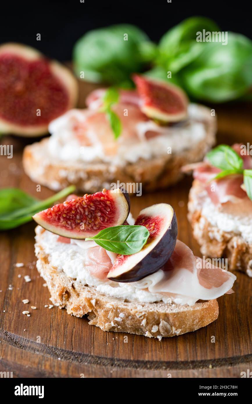 Toast bruschetta with ricotta, figs, ham on wooden serving board, closeup view. Gourmet snack Stock Photo
