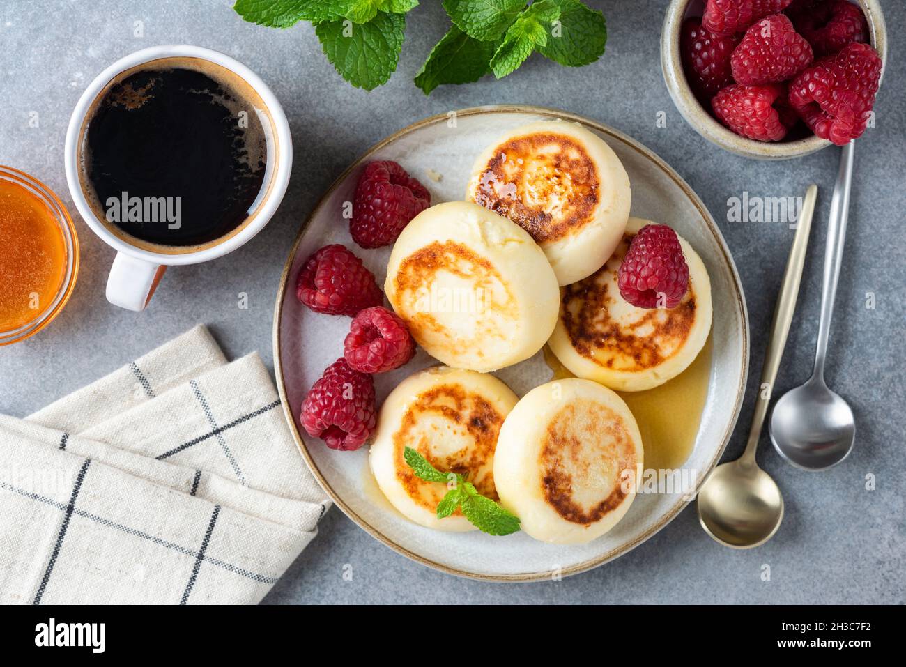 Curd cheese or cottage cheese fritters, syrniki served with honey, raspberries and cup of coffee. Table top view. Ukrainian, Russian cuisine breakfast Stock Photo
