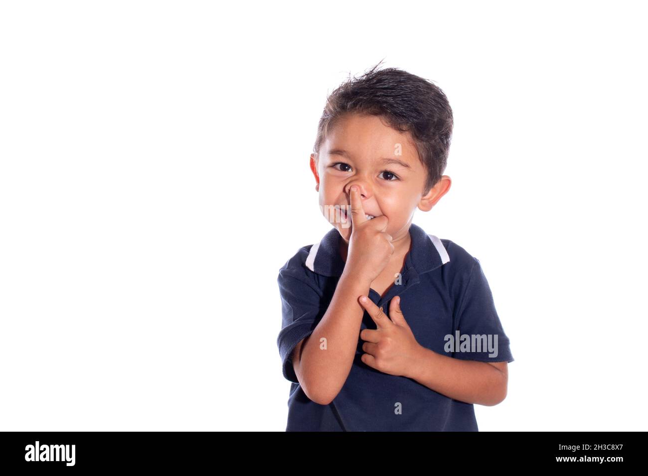 Embarrassed boy trying to pick his nose, isolated on white background. Latin child laughing while touching tip of his nose. Stock Photo