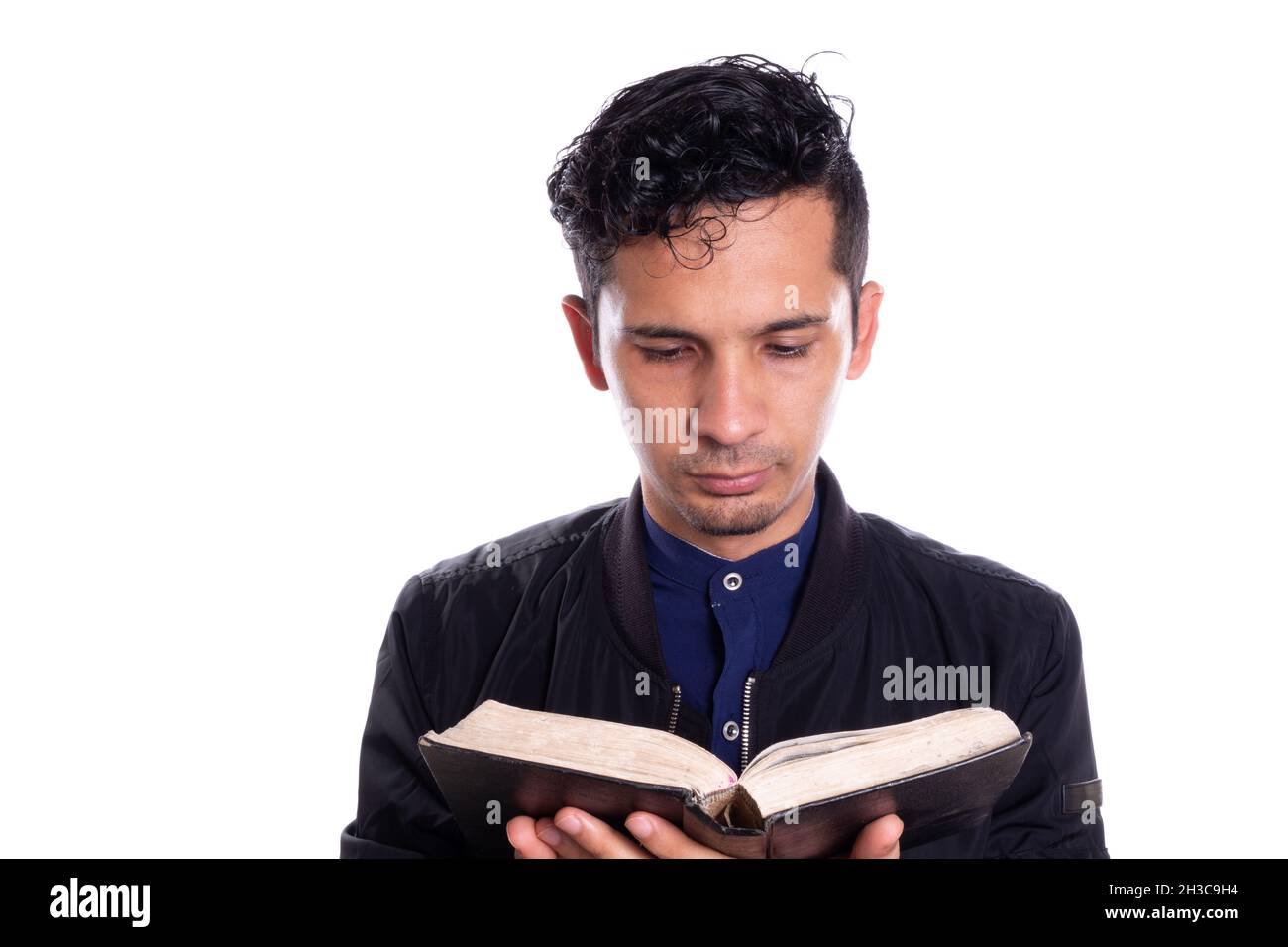Concentrated man reading a book, isolated on white background. Young adult latin young man reading and studying bible. Stock Photo