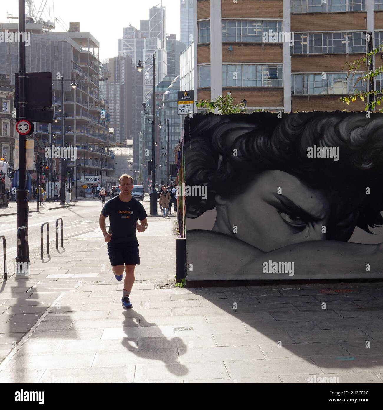 London, Greater London, England, October 26 2021: A man runs past Street art in Shoreditch with skyscrapers in the background. Stock Photo