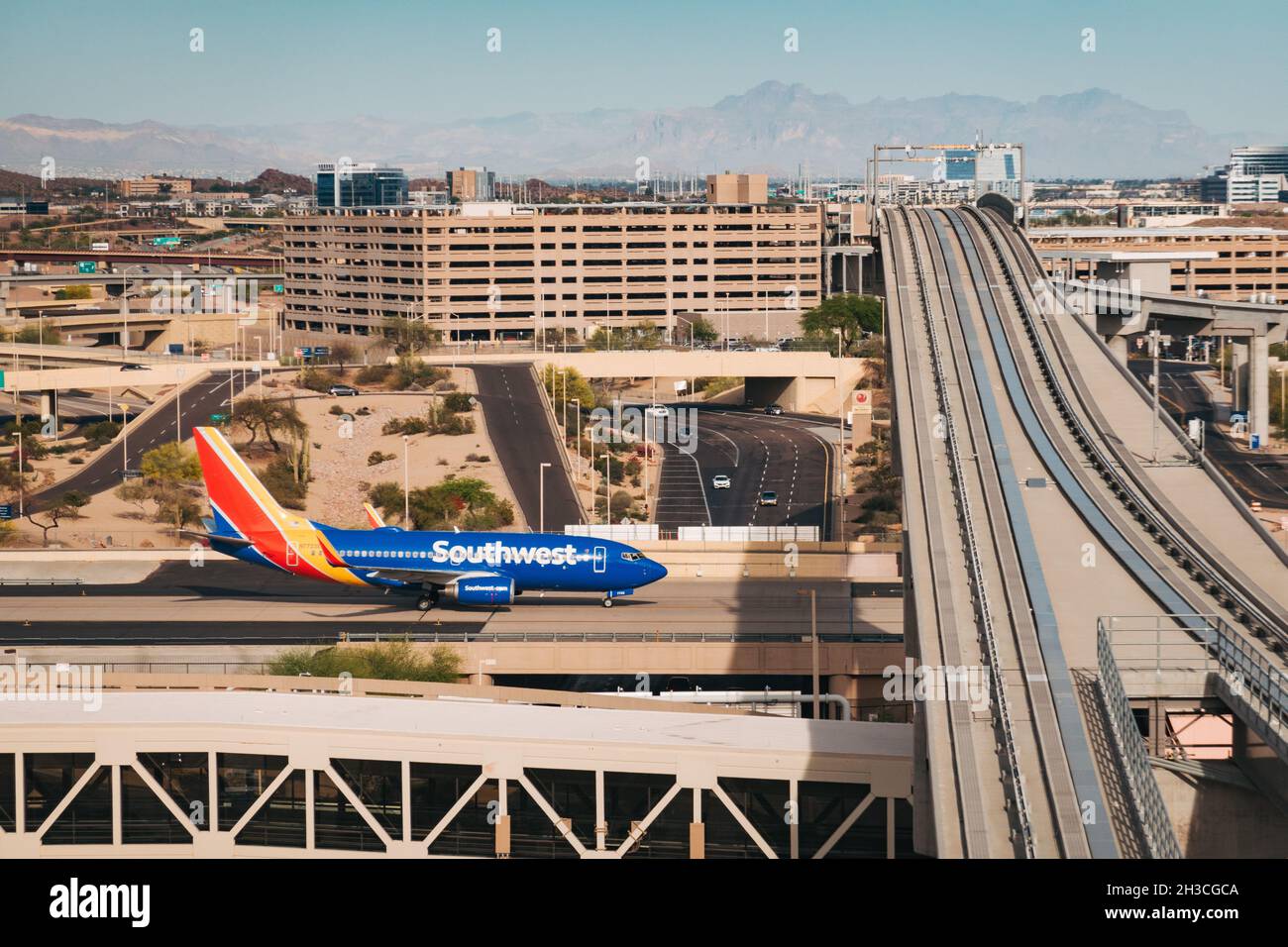 a Southwest Airlines Boeing 737 jet taxis under the PHX Sky Train tracks at Phoenix Sky Harbor Airport, Arizona, USA Stock Photo