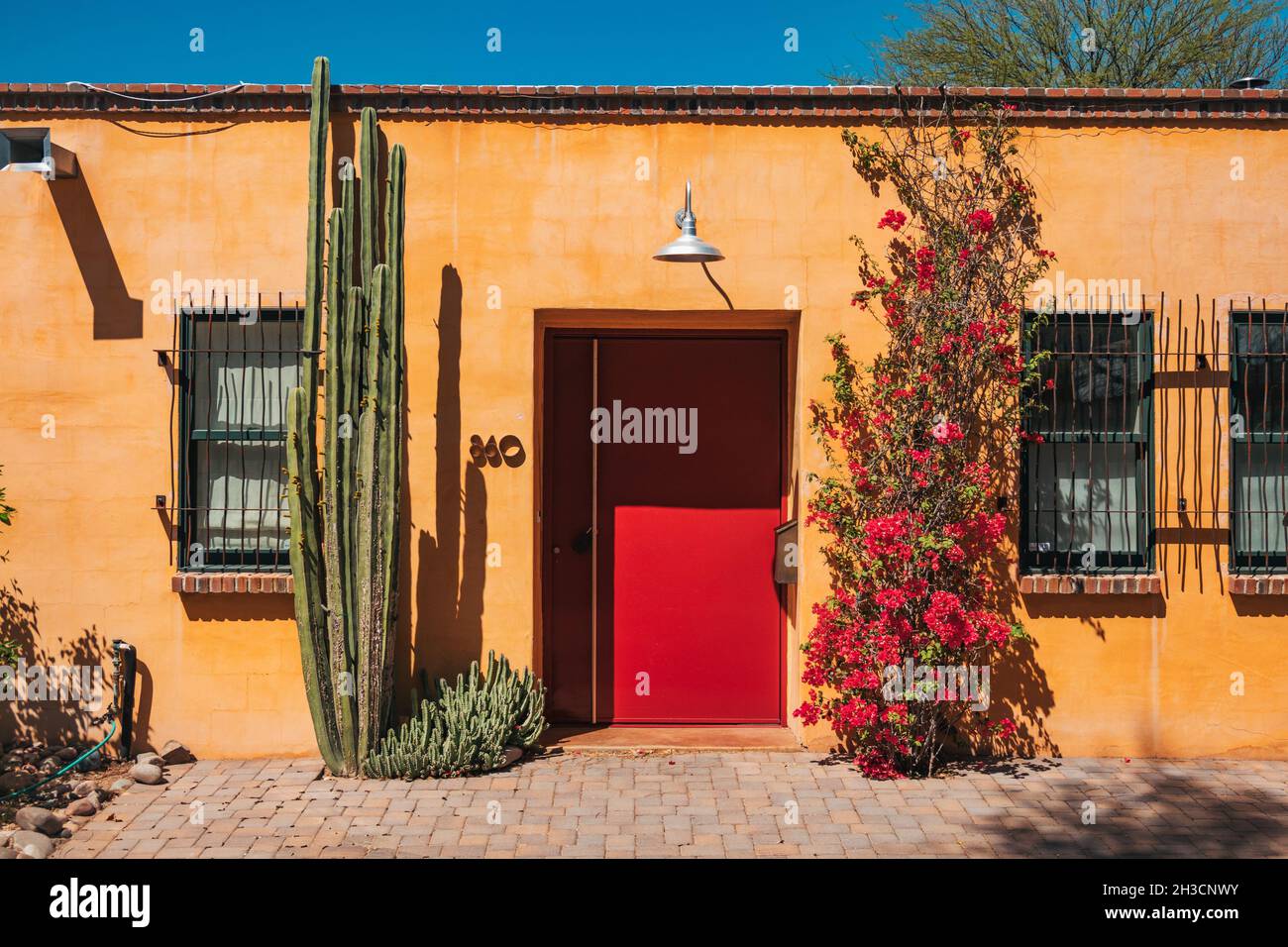 A large red metal door strikes a contrast with the yellow adobe