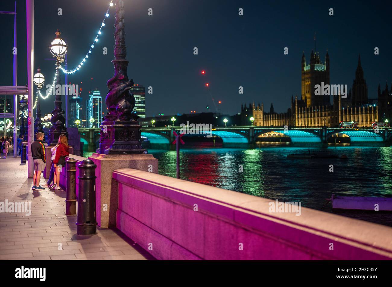 LONDON - SEPTEMBER 14, 2021: Colourfully lit night scene on The Queen's Walk, Southbank outside County Hall. Westminster Bridge and The Houses of Parl Stock Photo