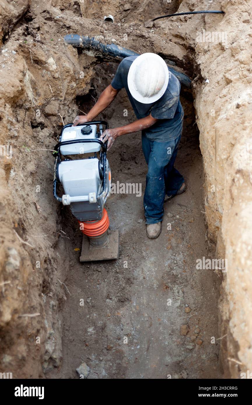 Construction worker operating a soil compactor in a deep trench Stock Photo