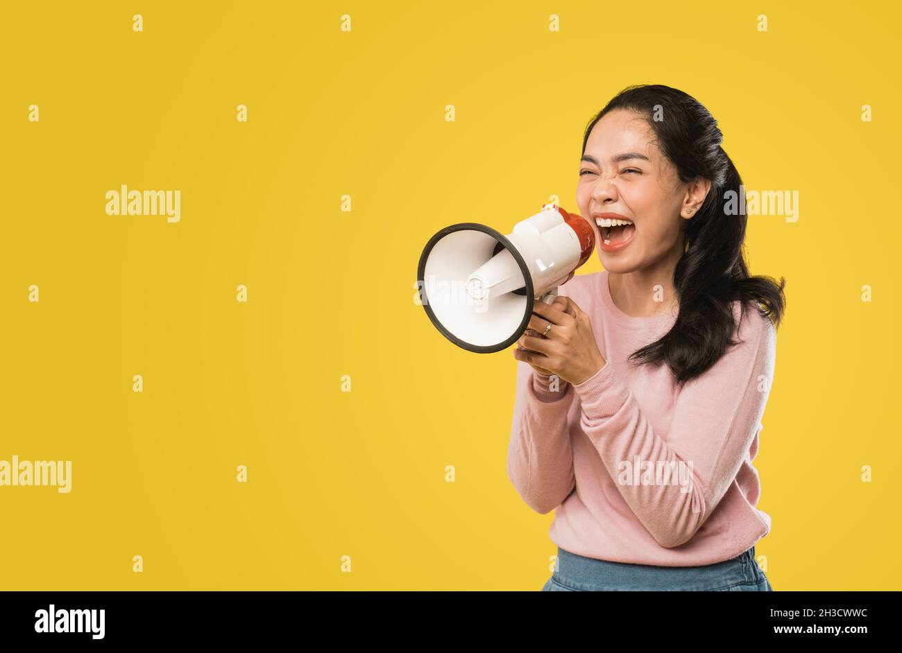 Asian woman screaming while holding megaphone with two hands making announcement Stock Photo
