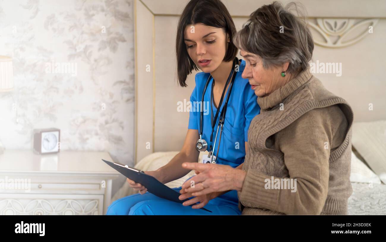 Young nurse is caring for an elderly 80-year-old woman at home,  Stock Photo