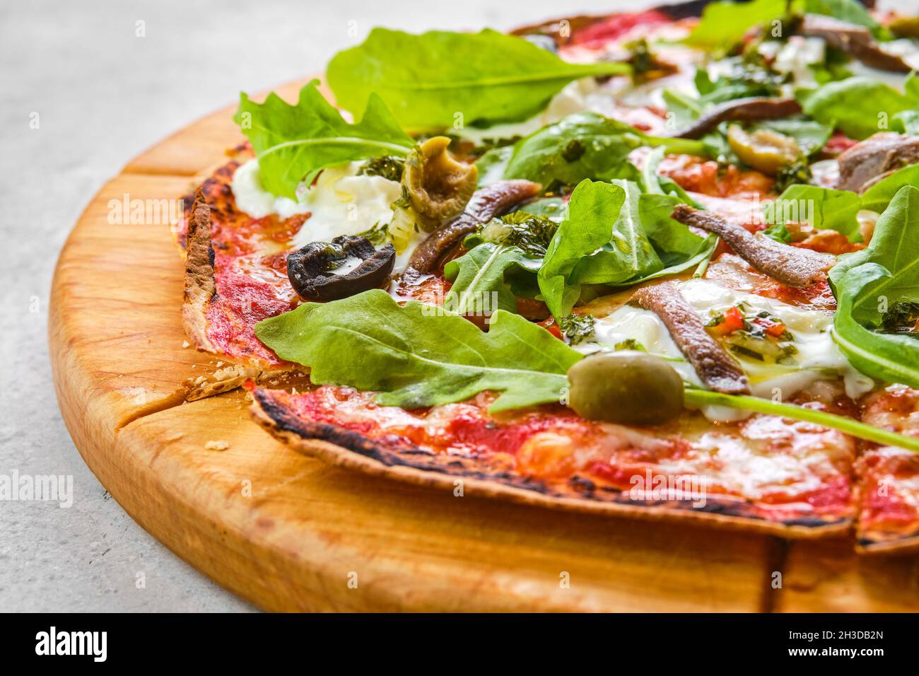 Thincrust pizza dough with anchovies, olives and stracciatella cheese (closeup photo with