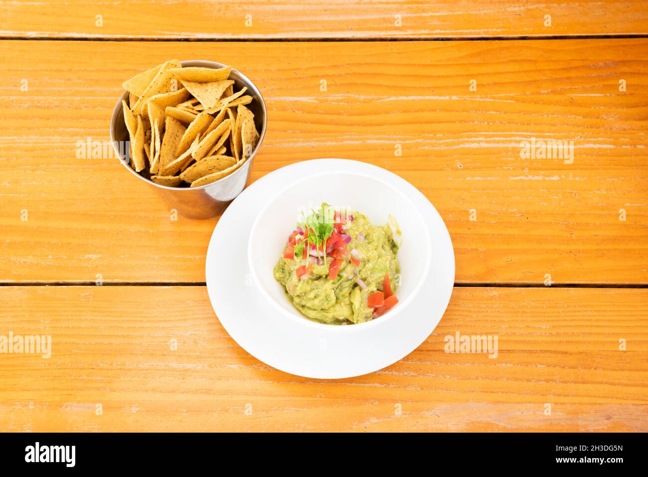 Plate of fresh Mexican guacamole with corn chips, parsley and tomato Stock Photo