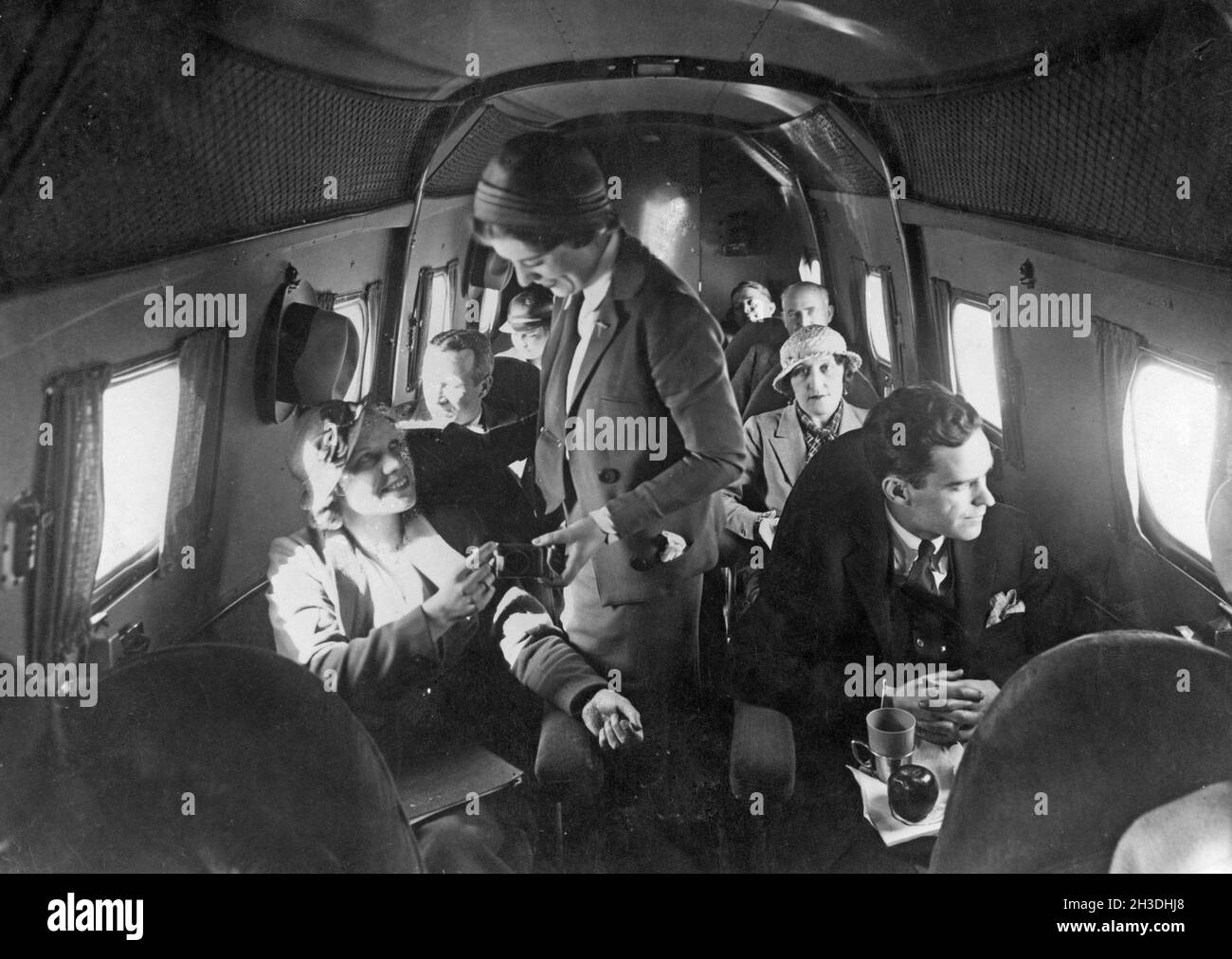 Airline travelling in the 1930s. A group of women and  men on an american passenger airplane in the 1930s. The female flight attendant is standing in the middle of the airplane servicing a young woman. Stock Photo