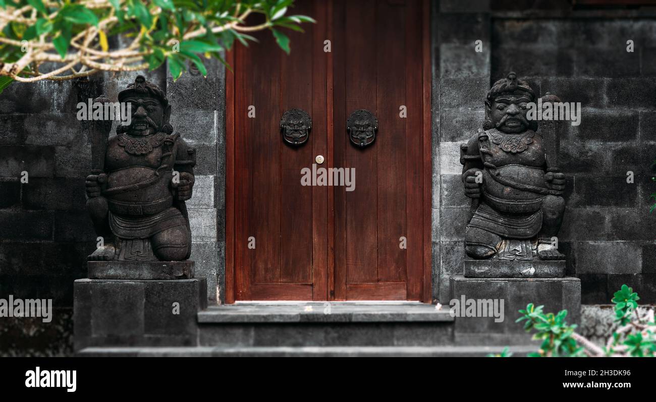 Door or gate to enter into traditional balinese garden architecture detail. Wooden Indonesian gate guarded by stone statues. Old wooden door, entrance Stock Photo