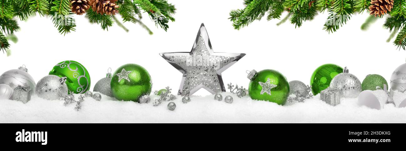Christmas decoration with stars and baubles in silver and green, arranged on snow below hanging fir branches, symmetrical, isolated on white backgroun Stock Photo