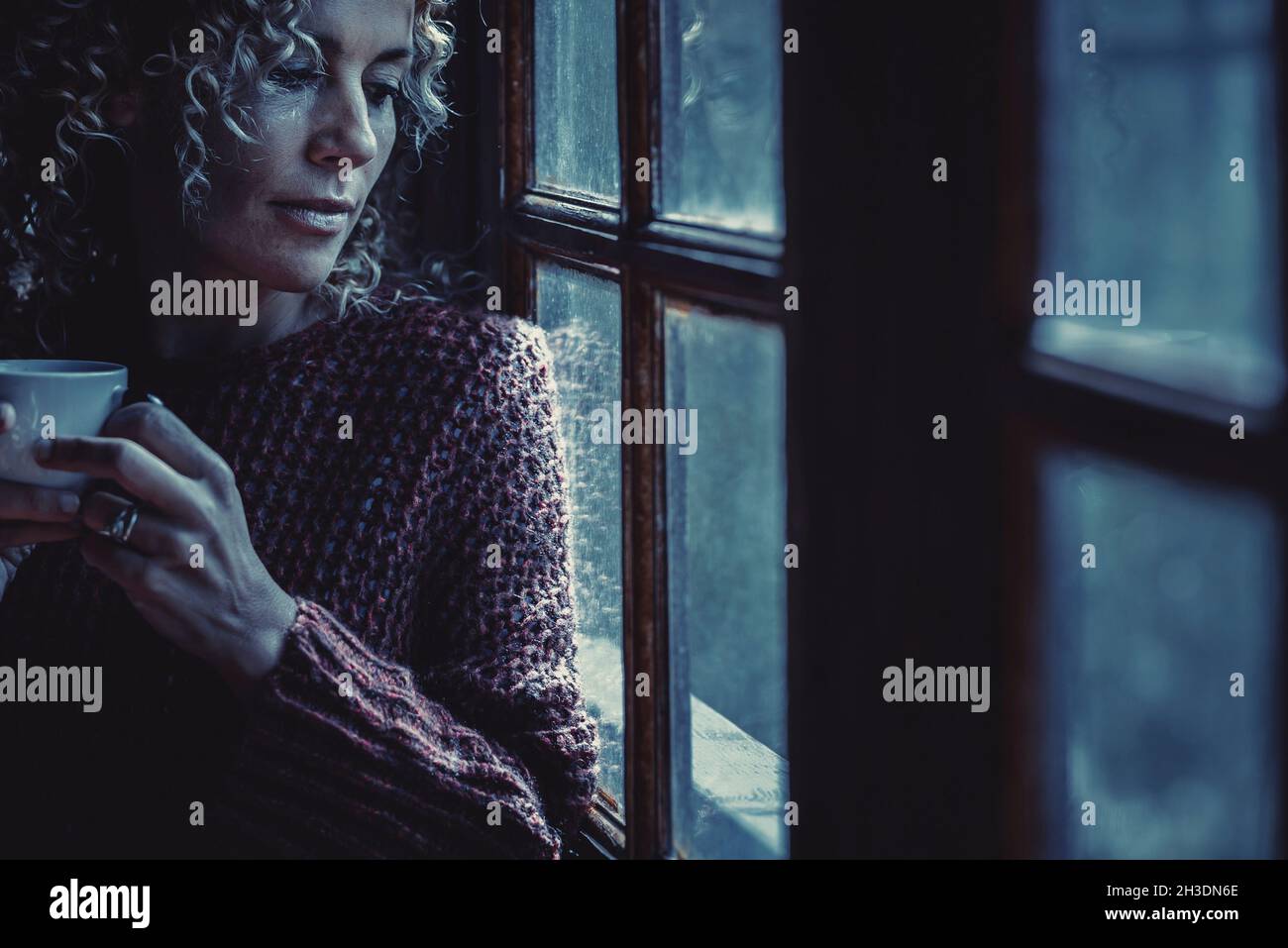 Blue tones lonely woman portrait looking outside the windows at home  drinking tea at the night. Concept of sadness and insomnia disease.  Attractive ad Stock Photo - Alamy