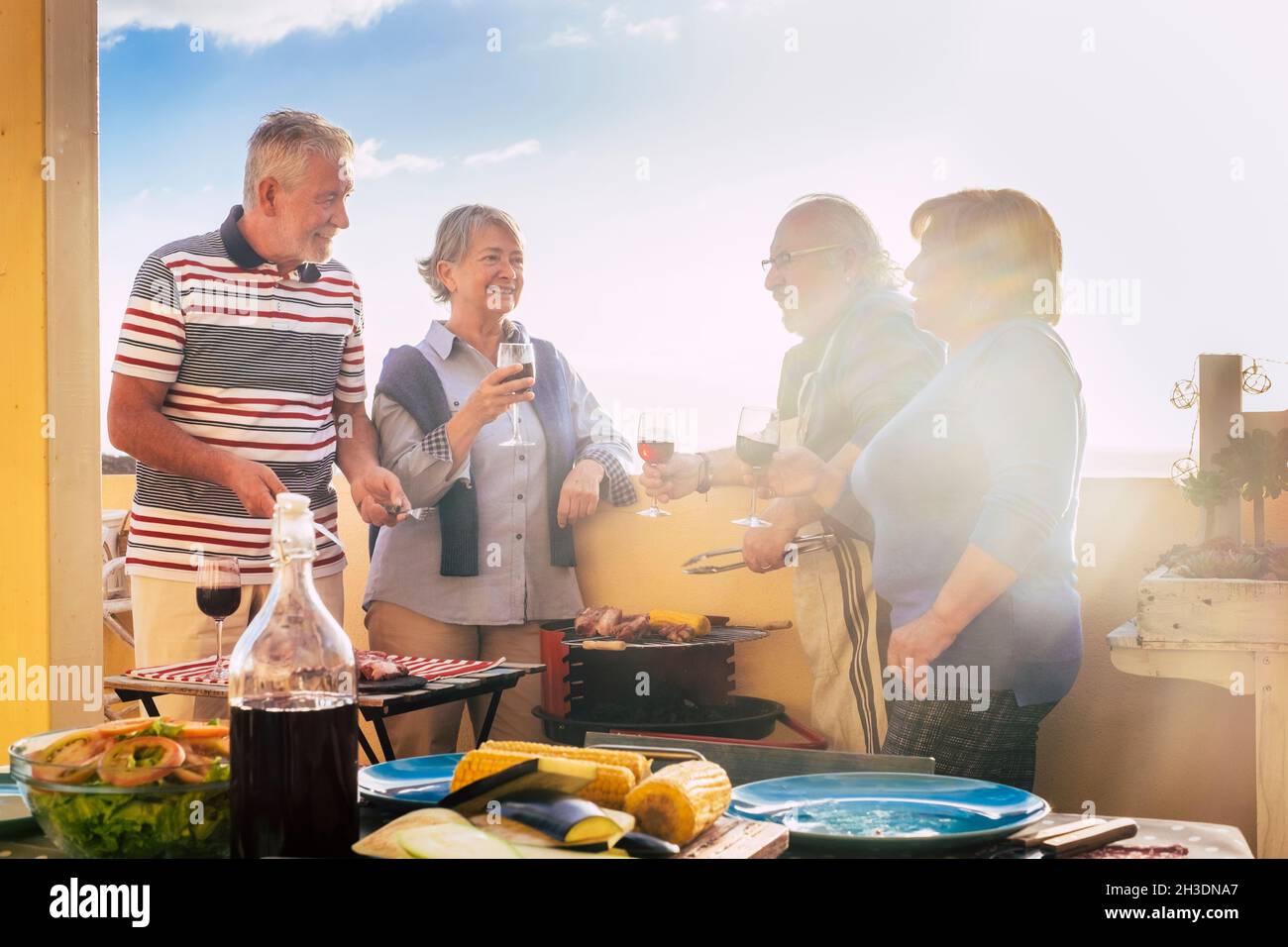 Group of elderly people have fun in frienship outdoor cooking a bbq all together. Senior couples friends enjoy leisure time eating and drinking and ce Stock Photo