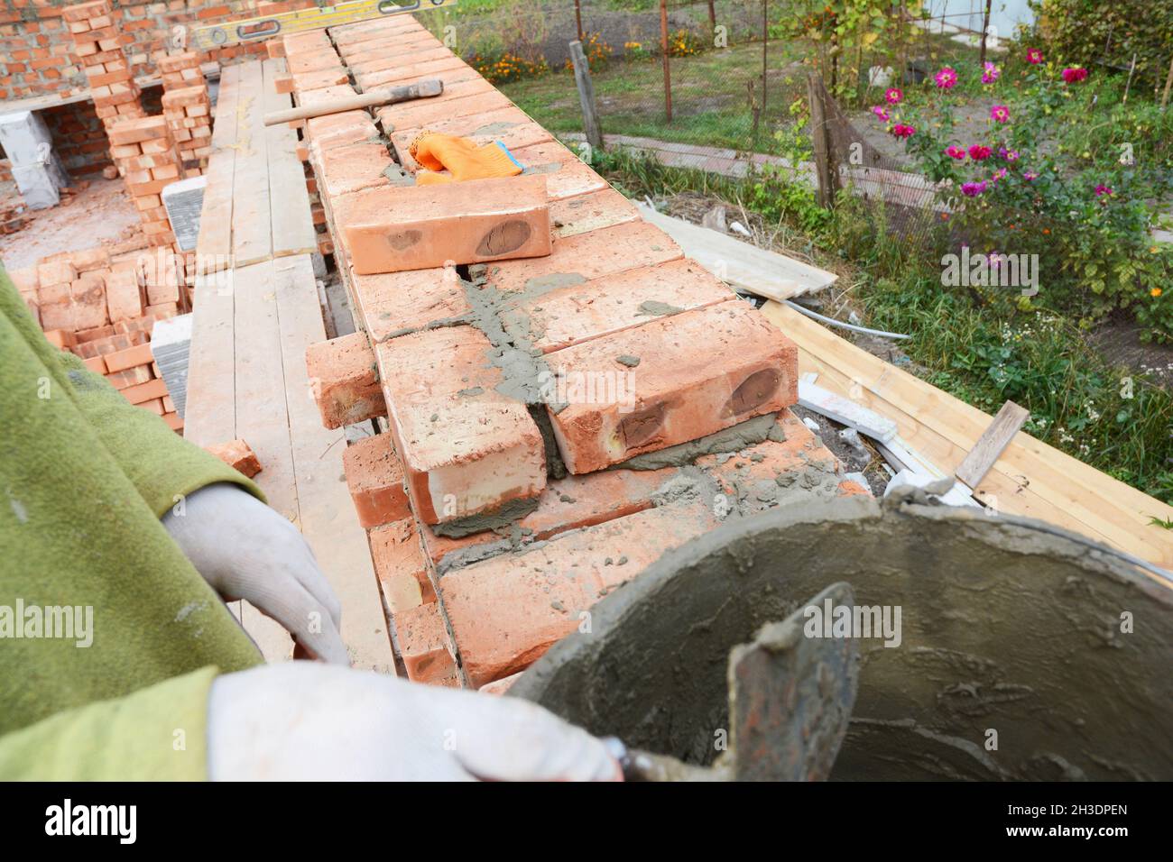Bricklayer worker installing red blocks and caulking brick masonry ...