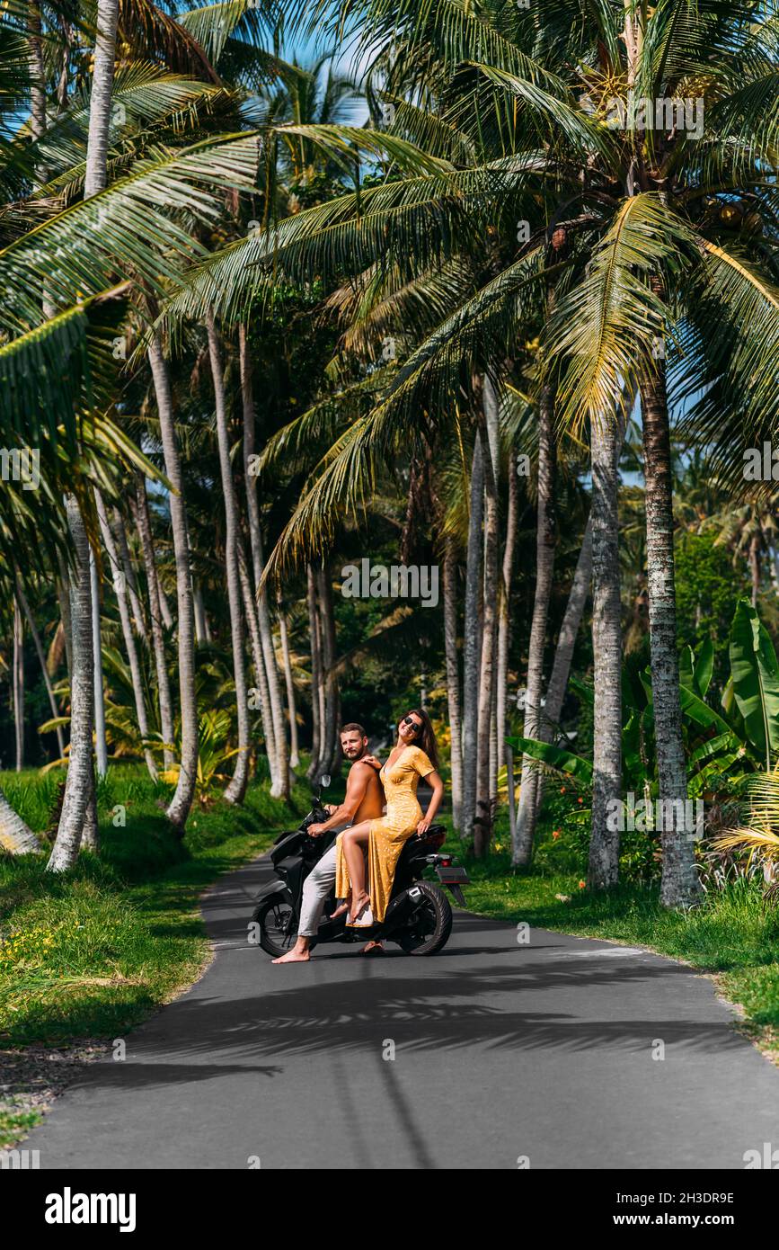 A couple in love on a scooter among the palm trees. Happy couple on vacation in Bali. The couple travels the world. Vacation in Asia. Traveling Stock Photo