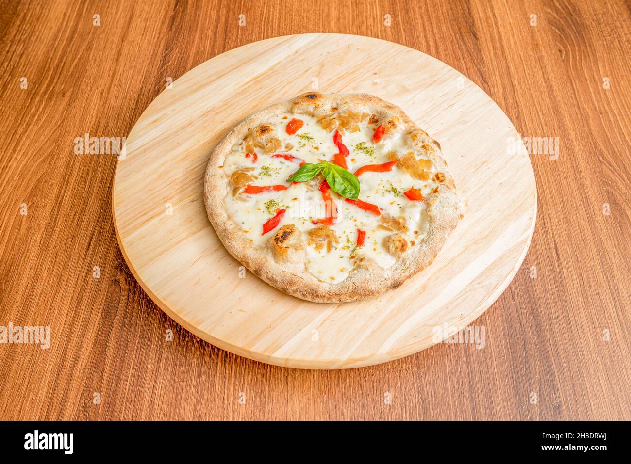 Small pizza with lots of melted mozzarella cheese, strips of roasted oregano red peppers and confit onion on round board Stock Photo