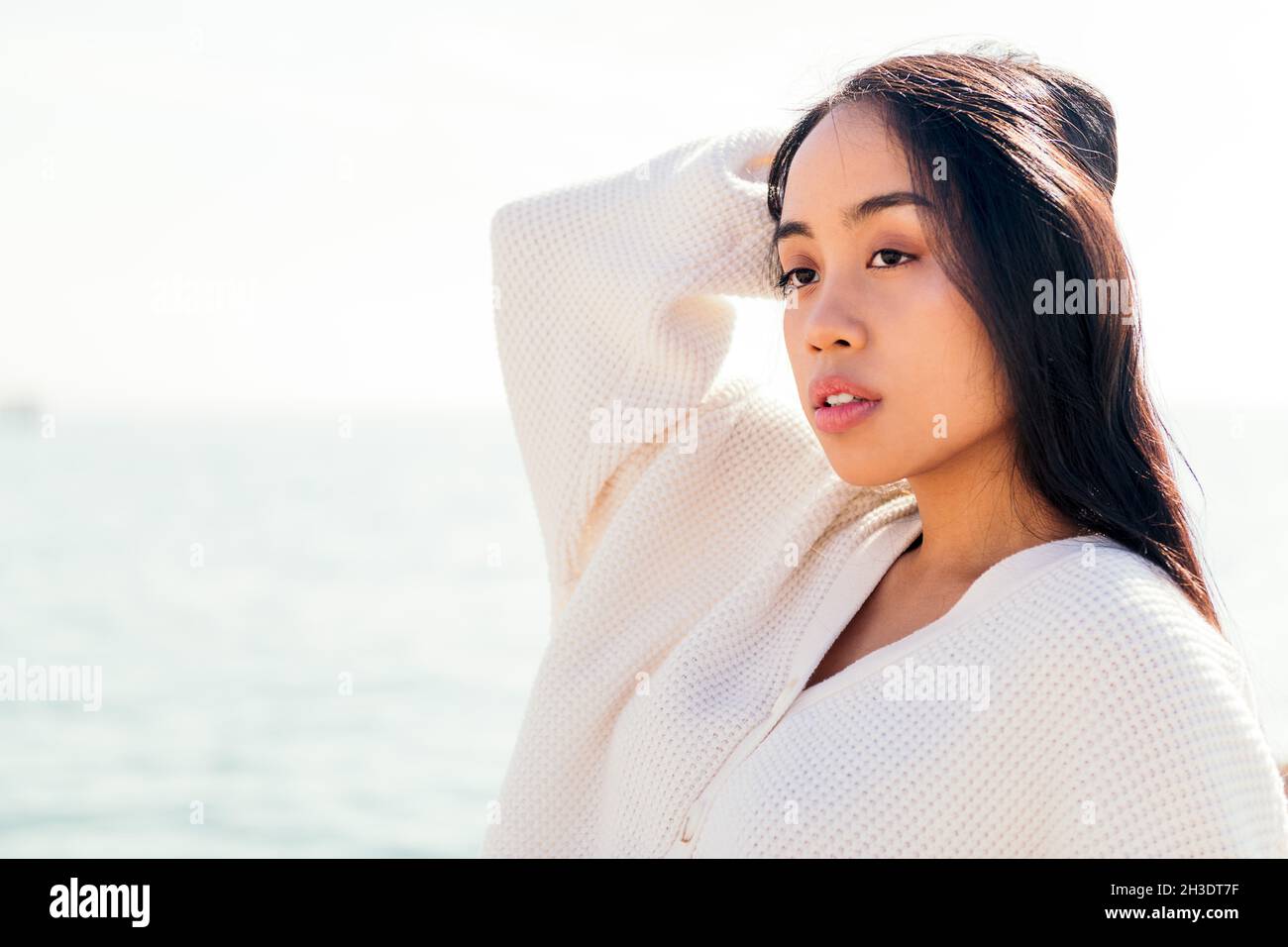 serious young asian woman in white touching her hair, concept of beauty ...
