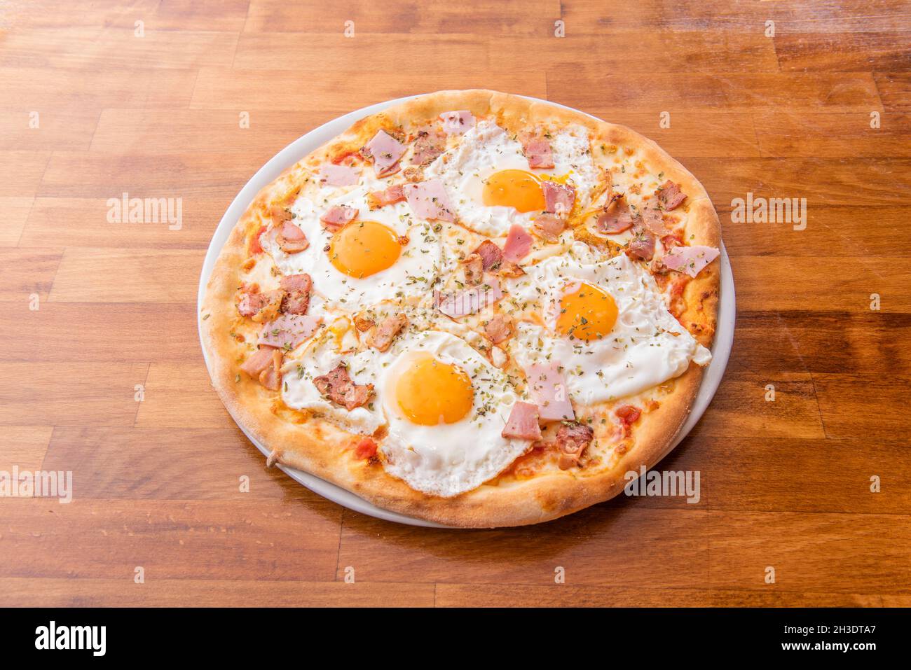 Pizza with four fried eggs with yellow yolks for dipping bread with pieces of ham and chicken with oregano Stock Photo