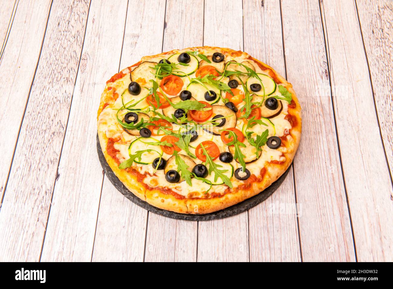 Vegan pizza with potato cheese with arugula, aubergine slices, black olive slices, cherry tomato slices, zucchini slices and tomato Stock Photo