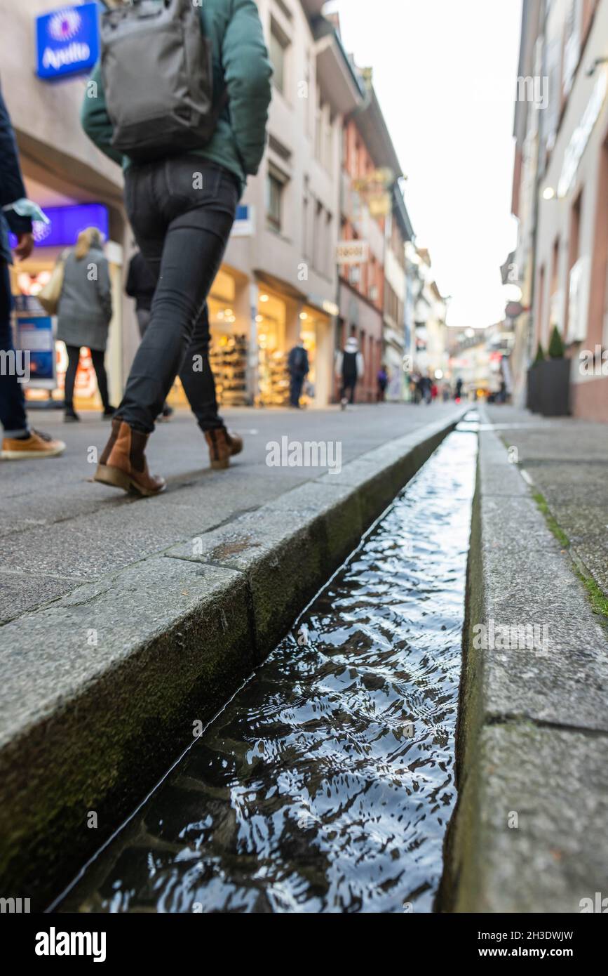 Freiburg, Germany. 27th Oct, 2021. Passers-by walk past the so-called  "Bächle". The small canals are one of the landmarks of the city and  provided in the Middle Ages for the irrigation and