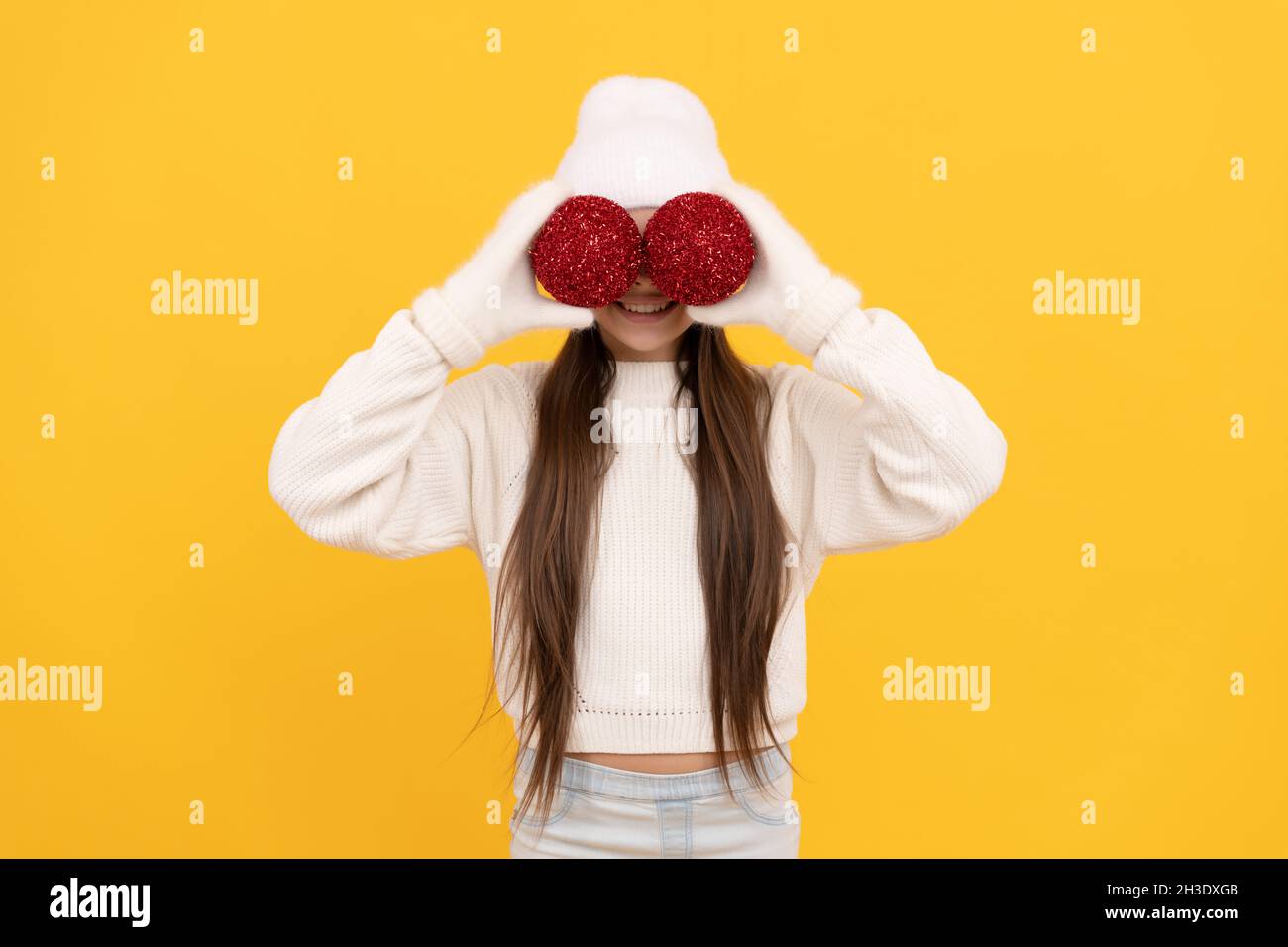 funny teen girl ion winter hat and gloves hold decorative christmas balls on yellow background, xmas Stock Photo