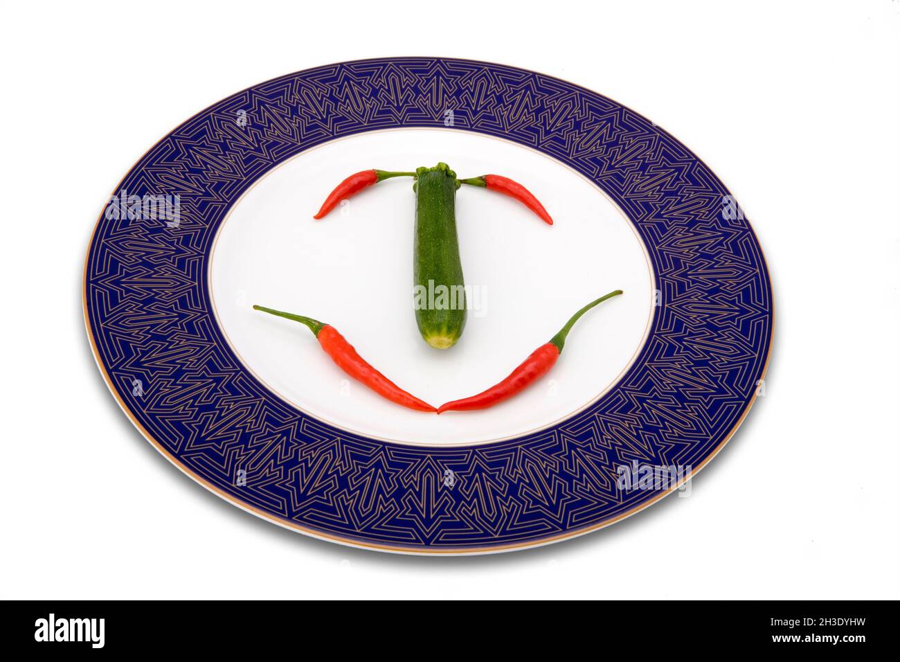 courgette, zucchini (Cucurbita pepo var. giromontiia, Cucurbita pepo subsp. pepo convar. giromontiina), and chilies arranged to a face on a plate Stock Photo