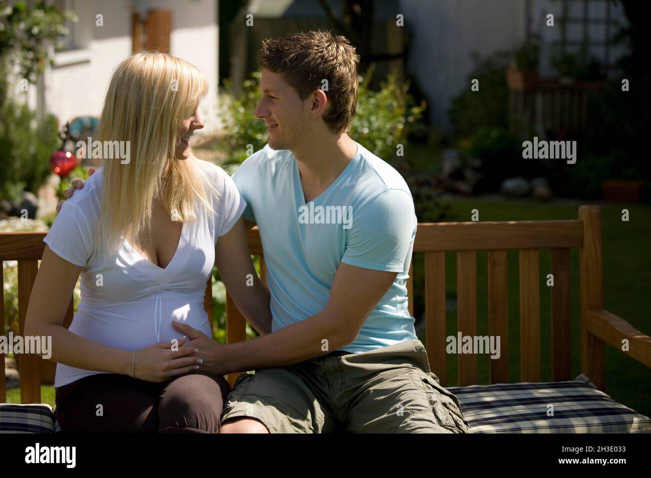 young parents-to-be sit on a bench full of anticipation and looking at each other in love Stock Photo