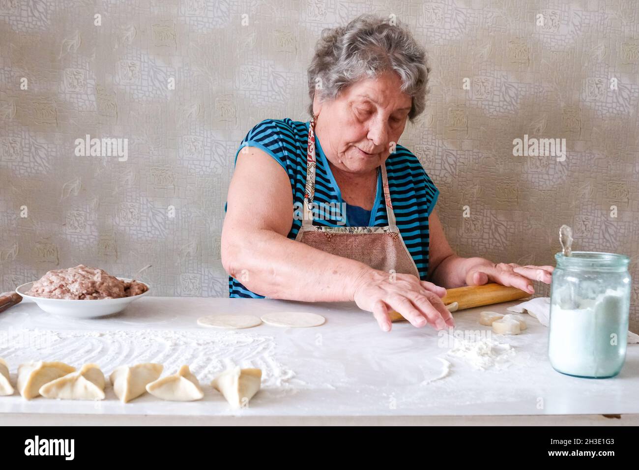 Grandmother makes manti, rolls dough for a dish Stock Photo