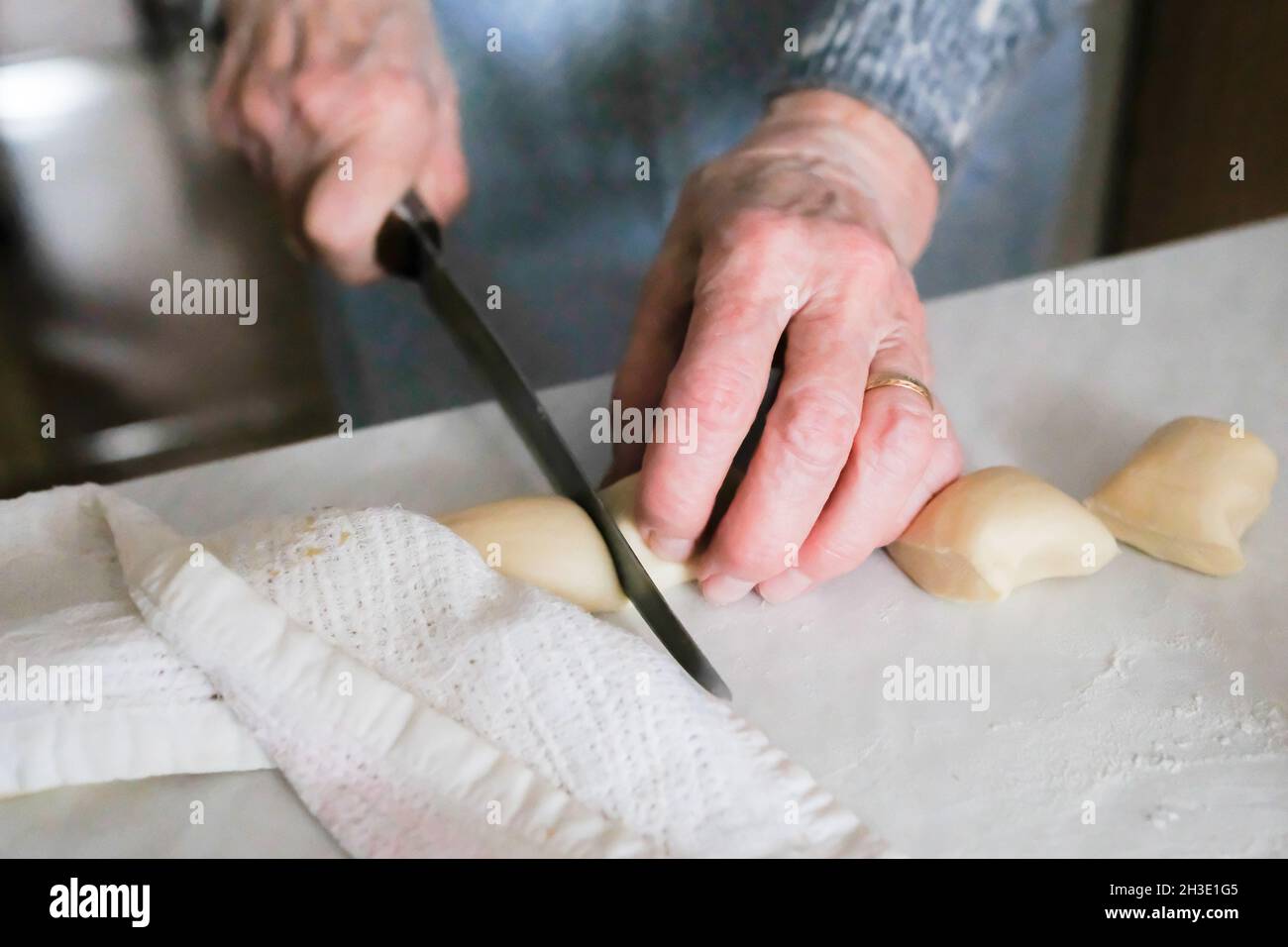 Grandmother cuts a bar of raw dough for making manti Stock Photo