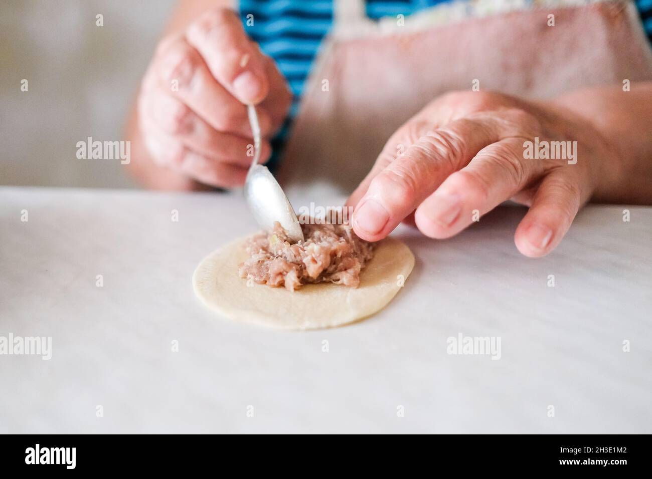 Grandmother spreads the meat on a thin piece of dough. Cooking manti or dumplings Stock Photo
