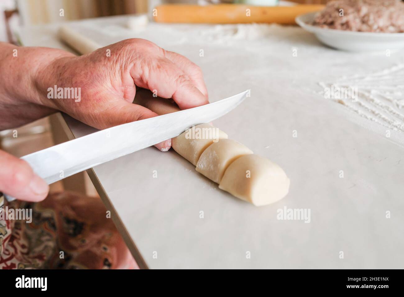 Grandmother cuts a bar of raw dough for making manti Stock Photo