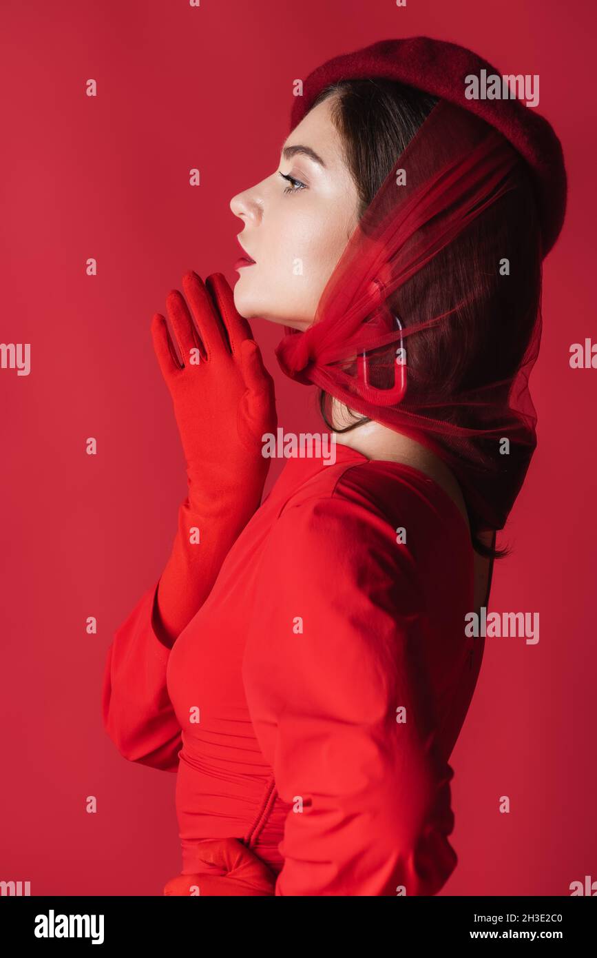 side view of elegant young woman in beret and dress isolated on red