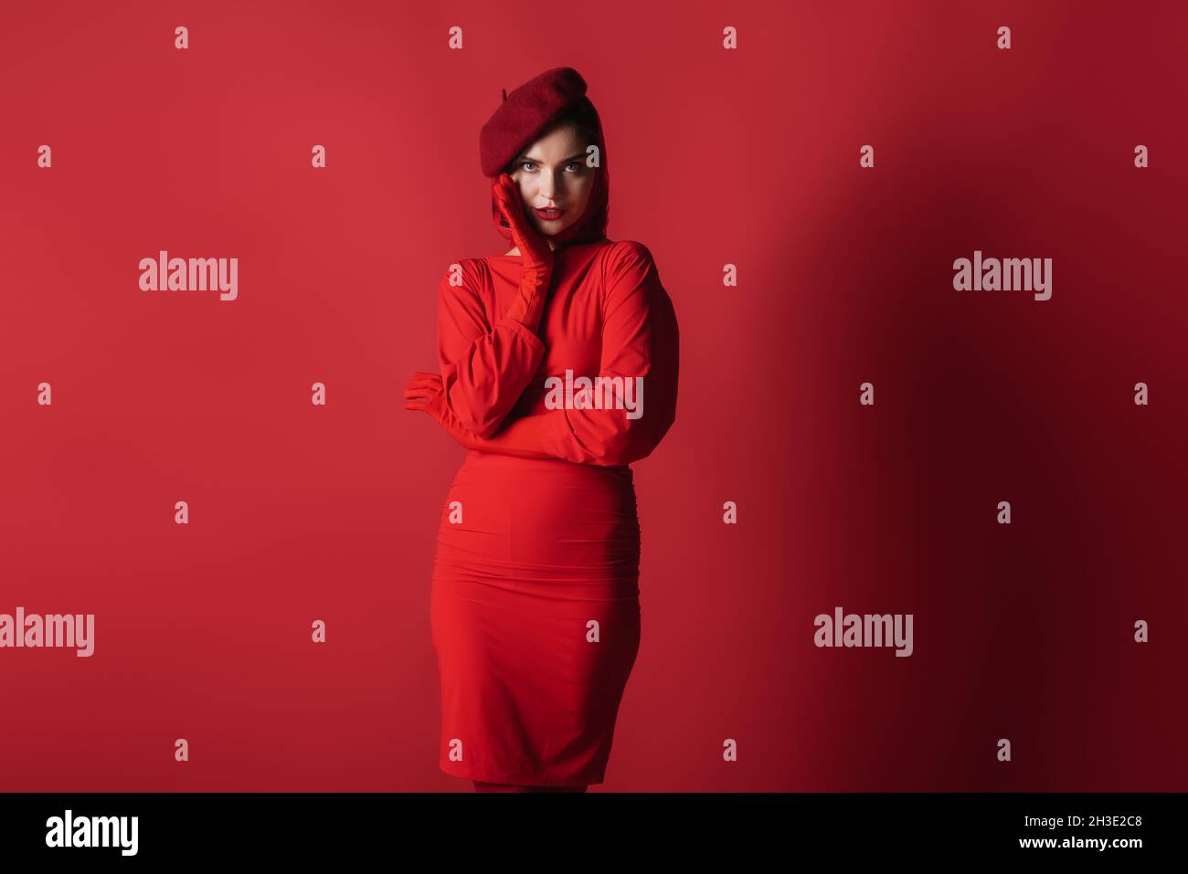 young elegant woman in beret and dress posing while looking at camera on red Stock Photo Alamy