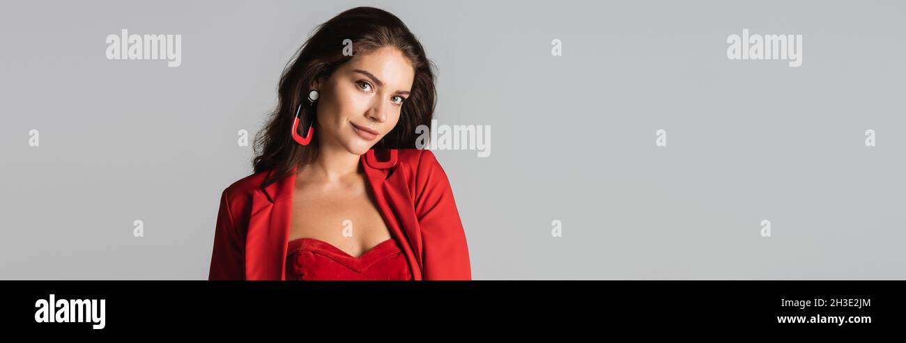 young trendy woman in red suit and earrings posing isolated on grey, banner Stock Photo