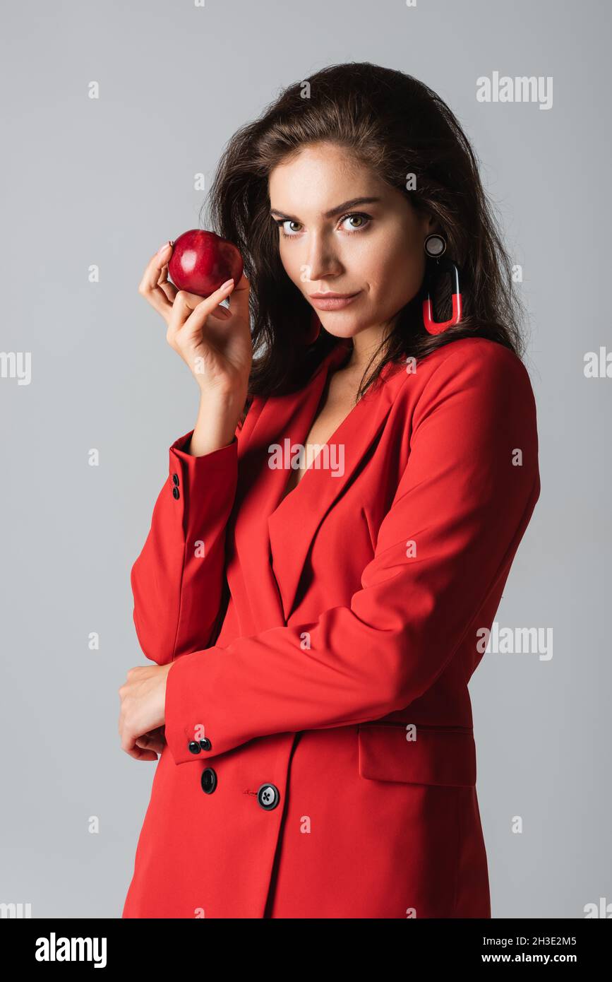 young stylish woman in red suit posing with ripe apple isolated on grey Stock Photo