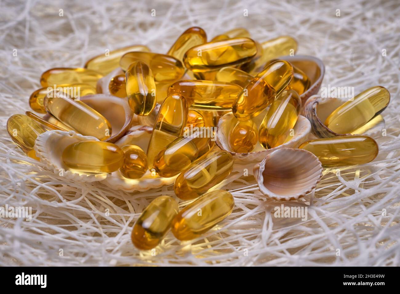 Omega-3 fish fat oil capsules heap lie on the small shells and fishing net. EPA and DHA are essential fatty substances that our bodies need on a daily Stock Photo