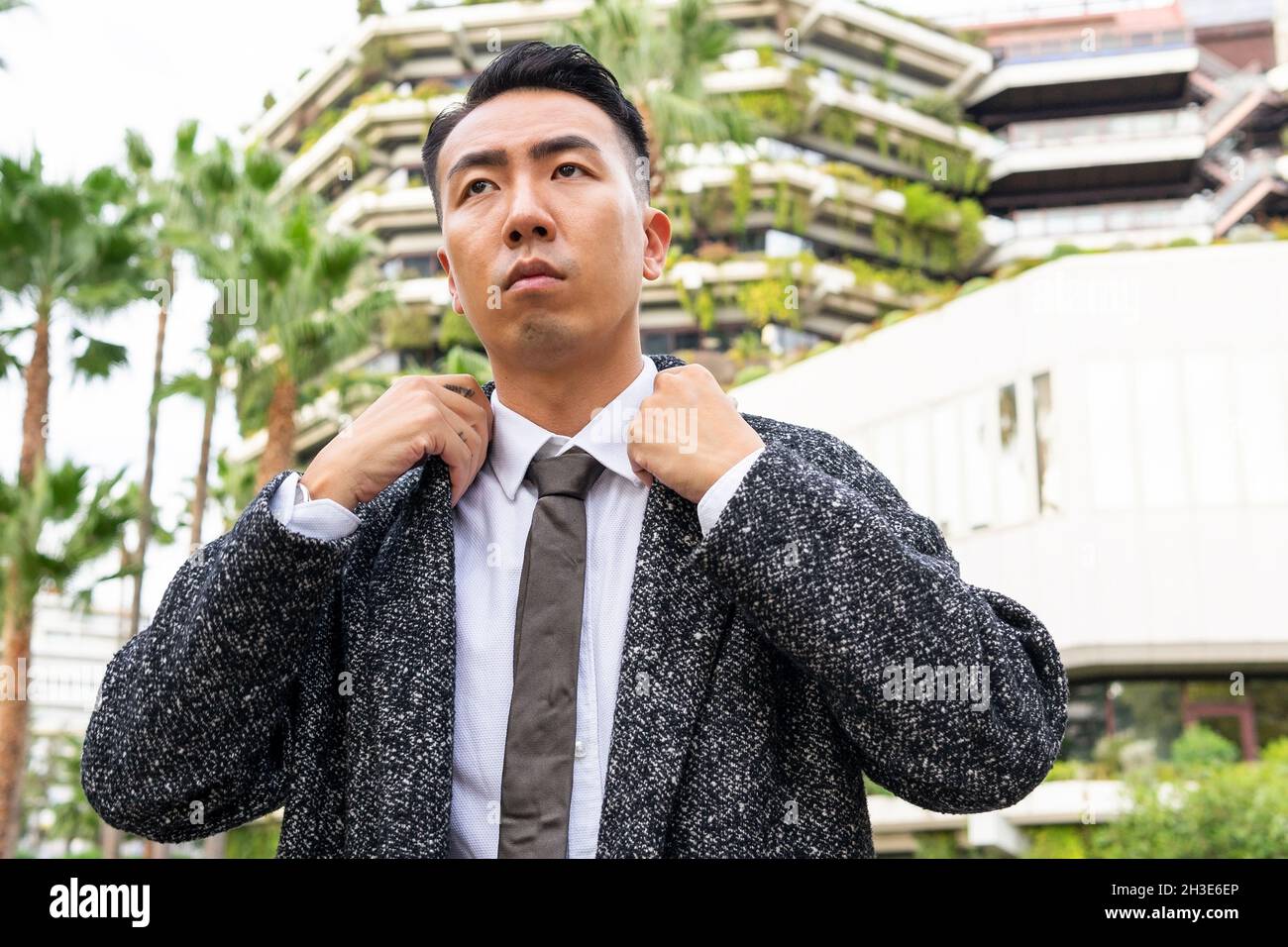 Well dressed young Asian male entrepreneur in tie looking away while strolling on road against modern buildings in city Stock Photo