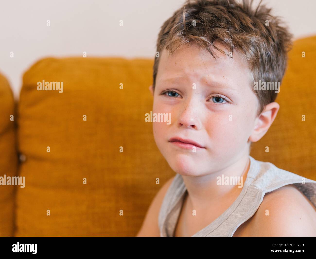 Unhappy ill child having cold and sitting on couch at home Stock Photo