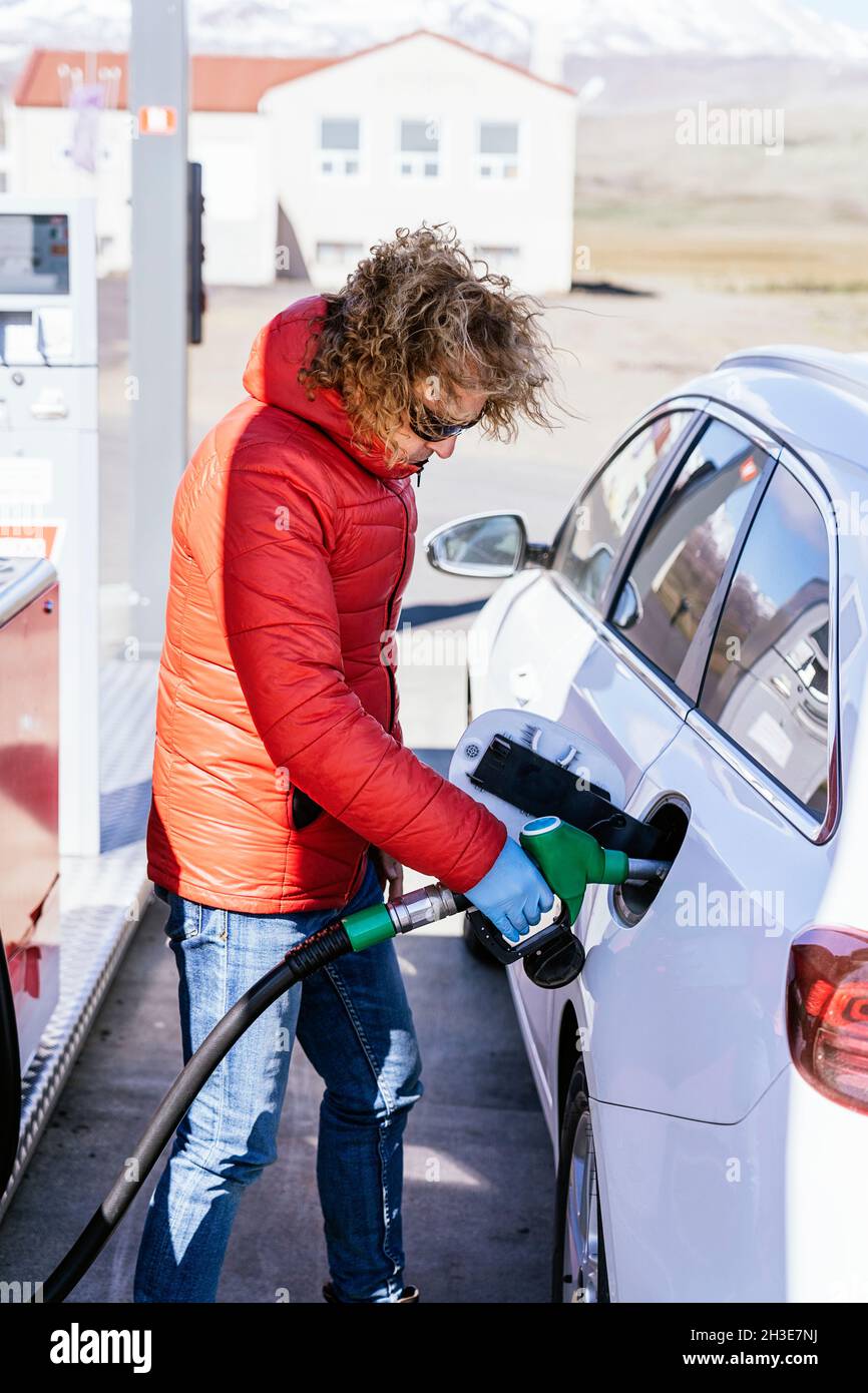 Side view of serious male with curly hair in outwear and latex gloves  standing while refueling car at gas station in sunny day Stock Photo - Alamy