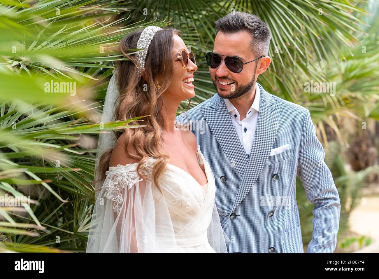 Smiling young married couple in wedding clothes and sunglasses standing
